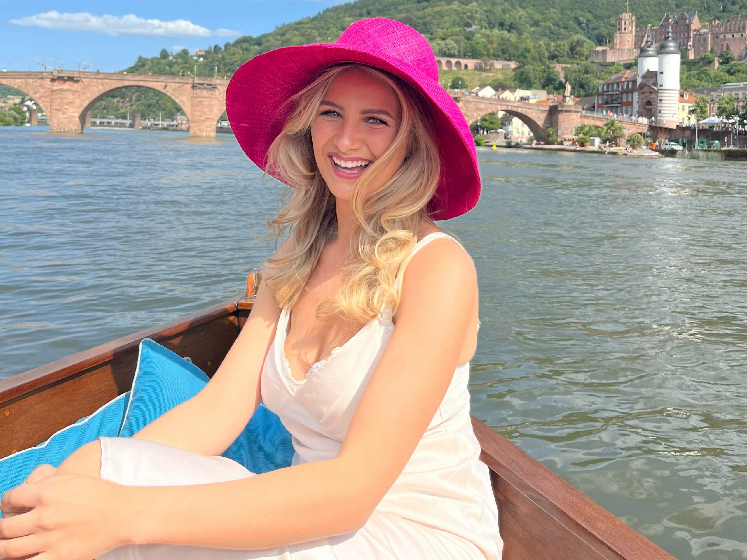 Eine Frau mit einem pinken Hut sitzt am Bug des Boots von Riverboat am Neckar