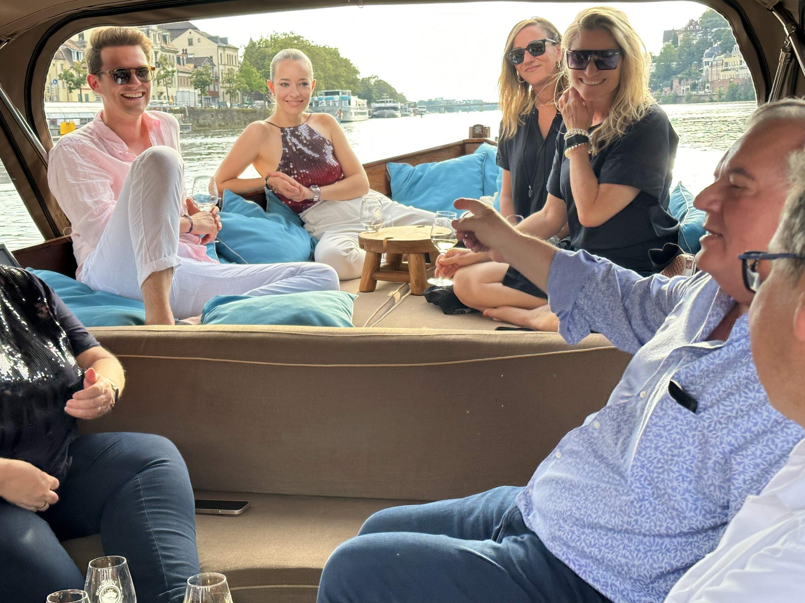 Arbeitskollegen sitzen bei einem Teambuilding am Bug und im Inneren des Boots von Riverboat, trinken Wein und unterhalten sich
